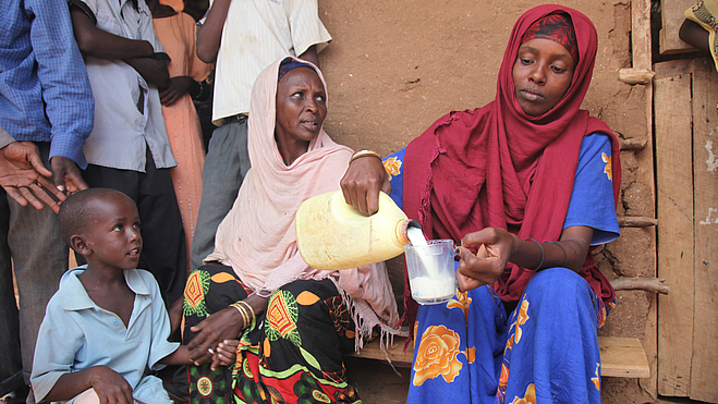 Pastoralistin verteilt Kamelmilch an Frauen und Kinder
