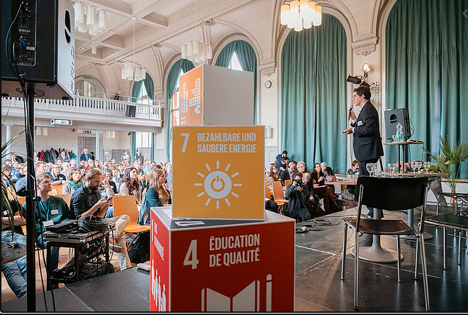 Bühne der SDSN Nachhaltigkeitskonferenz 2019 Würfel mit den aufgedruckten Nachhaltigkeitszielen 7 und 4 sieht man im Vordergrund