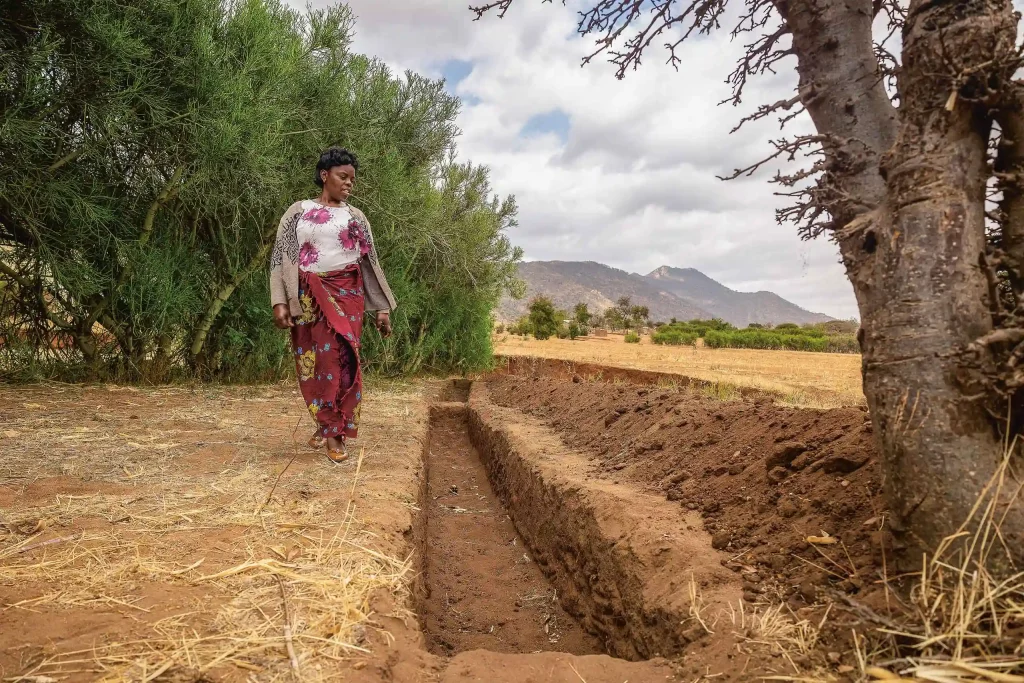 Eine Frau betrachtet ihren Graben gegen Erosion und zum Auffangen des Regenwassers.