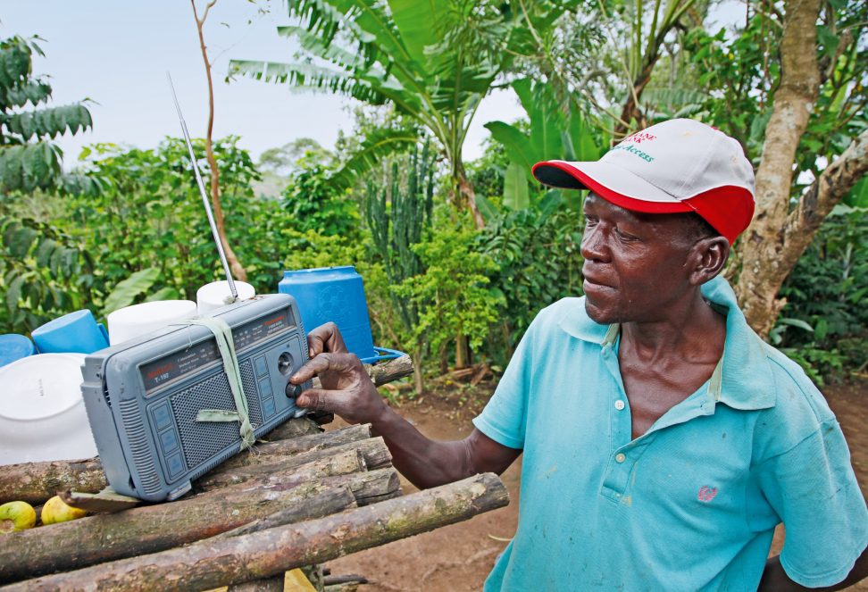 Ein Bauer stellt das Radio ein, um The Organic Farmer Radio vom Farmer Communication Programme zu hören.