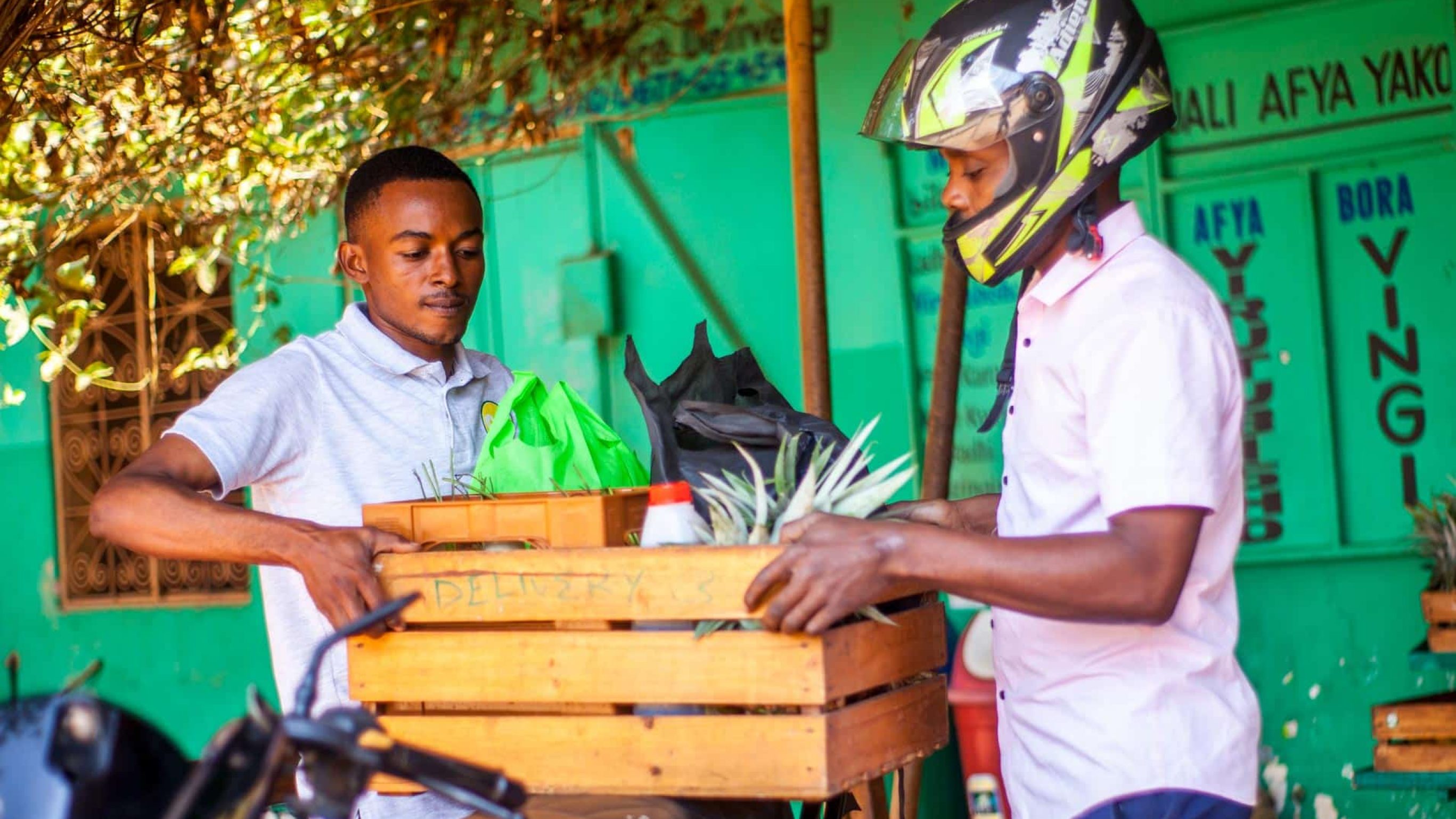Zwei Männer packen eine Kiste Gemüse auf ein Motorrad. Bild: Anold William.