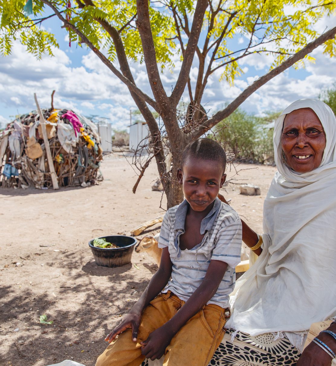 Bishar Dulo Witwe und sechsfache Mutter aus Boji in Kenia mit mit einem ihrer Enkelkinder im Schatten eines Baumes